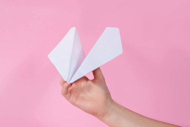 El ve kağıt uçak pembe arka planda. Çocuk oyun oynuyor. Çocuk umudu kavramı. Oyuncak bebek. seyahat beyaz uçak