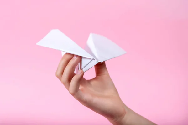 Hand and paper airplane on pink background. the child is playing. concept of children\'s hope. DIY toy. traveling white plane
