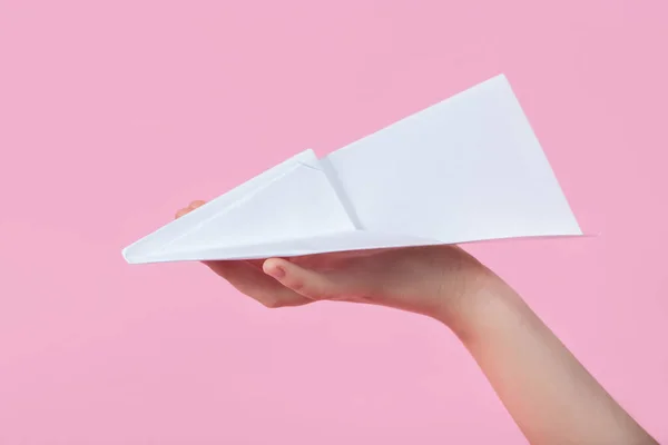 paper plane in the children\'s hand on a pink background. travel games with baby. concept of flying into the future. games without a smartphone. origami paper work. games at school