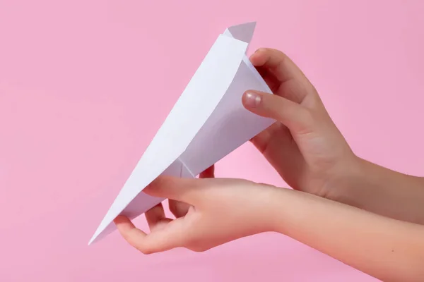 paper plane in the children's hand on a pink background. travel games with baby. concept of flying into the future. games without a smartphone. origami paper work. games at school