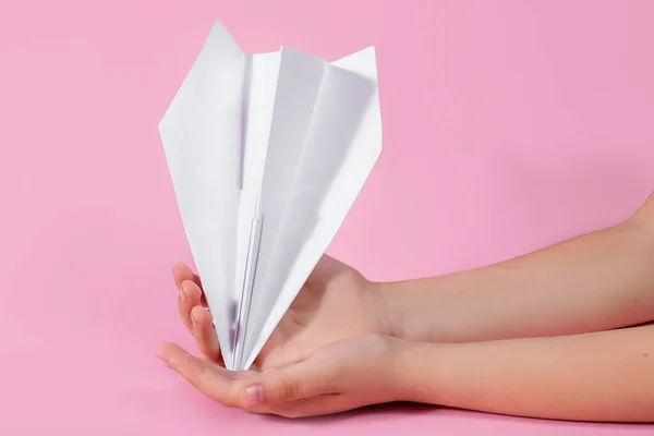 paper plane in the children's hand on a pink background. travel games with baby. concept of flying into the future. games without a smartphone. origami paper work. games at school