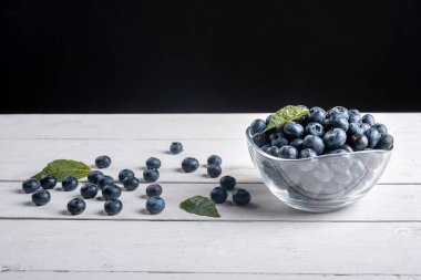 Beyaz bir masada siyah bir arka planı olan ve ahşap bir masaya serpiştirilmiş yaban mersini. Kırsal, sağlıklı yiyecek.