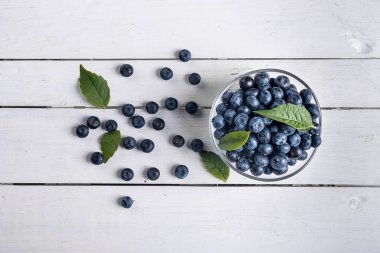 Beyaz ahşap bir masada siyah arka planı olan yabanmersinleri bir bardaktan dağılır. Taze yaz meyvesi.