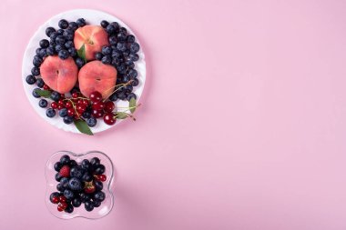 Pembe arka planda bir tabak yaz meyvesi. Bir bardak yaban mersini ve frenk üzümü.