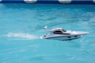 white boat in a blue pool splashing water. children's toy on radio control. water games in summer in sunny weathe
