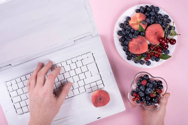 creative white laptop on trendy pink background with summer frui