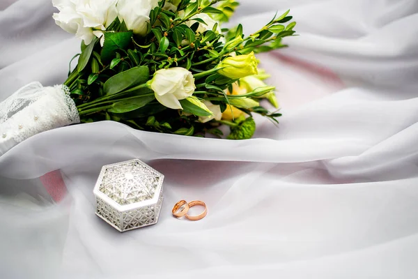 结婚戒指 一束鲜花和一个盒子躺在美丽的白色织物上 婚礼前的早上 活动机构的概念E — 图库照片