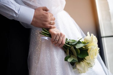 wedding theme. newlyweds hold hands with a bouquet and rings against the window in the studio. concept for event agencie