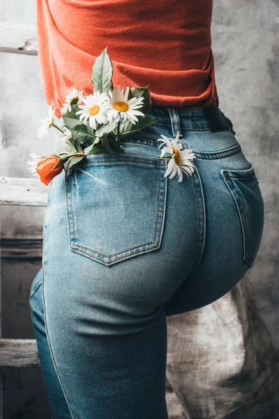 Blooming daisies in the back pocket. Woman posing with daisy flowers in jeans pocket on rustic background. The concept of sensuality and tendernes