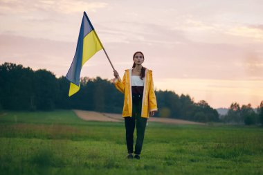 Ukraynalı kadın büyük bir Ukrayna bayrağıyla sahada. Vatansever fotoğraflar. Kahramanlık ve özgürlük. Kavram. Sarı yağmurluk giymiş güzel bir kadın. Seyahat