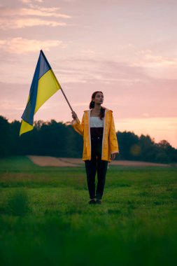 Ukraynalı kadın büyük bir Ukrayna bayrağıyla sahada. Vatansever fotoğraflar. Kahramanlık ve özgürlük. Kavram. Sarı yağmurluk giymiş güzel bir kadın. Seyahat