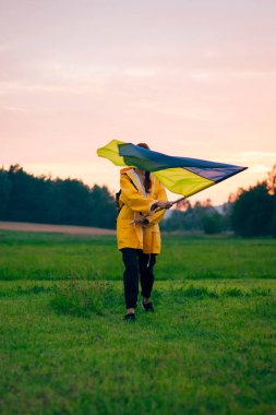 Ukraynalı kadın büyük bir Ukrayna bayrağıyla sahada. Vatansever fotoğraflar. Kahramanlık ve özgürlük. Kavram. Sarı yağmurluk giymiş güzel bir kadın. Seyahat