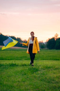 Ukraynalı kadın büyük bir Ukrayna bayrağıyla sahada. Vatansever fotoğraflar. Kahramanlık ve özgürlük. Kavram. Sarı yağmurluk giymiş güzel bir kadın. Seyahat