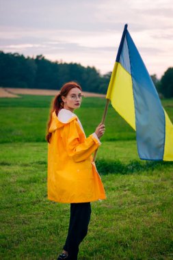Ukraynalı kadın büyük bir Ukrayna bayrağıyla sahada. Vatansever fotoğraflar. Kahramanlık ve özgürlük. Kavram. Sarı yağmurluk giymiş güzel bir kadın. Seyahat