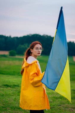 Ukraynalı kadın büyük bir Ukrayna bayrağıyla sahada. Vatansever fotoğraflar. Kahramanlık ve özgürlük. Kavram. Sarı yağmurluk giymiş güzel bir kadın. Seyahat