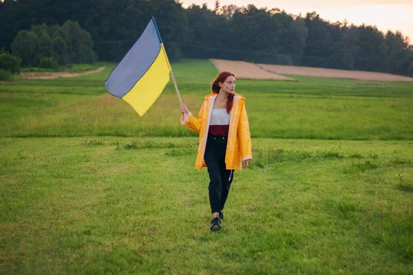 Ukraynalı kadın büyük bir Ukrayna bayrağıyla sahada. Vatansever fotoğraflar. Kahramanlık ve özgürlük. Kavram. Sarı yağmurluk giymiş güzel bir kadın. Seyahat