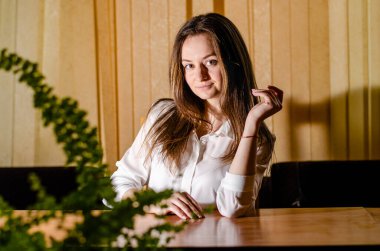 Masanın önünde beyaz gömlekli güzel bir kızın yatay portresi..