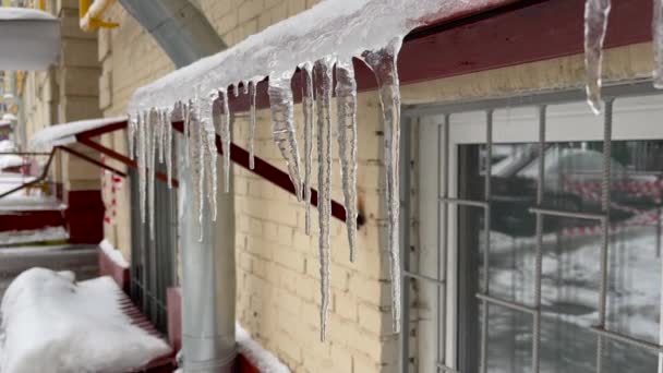 Lange ijspegel die aan de dakrand hangt en smelt. Er lopen druppels water door de smeltende ijspegel. Voorjaarsthema. — Stockvideo