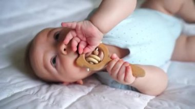Üç aylık, tahta doğal çıngıraklı şirin bir bebek, yatakta yatıyor, diş çıkarma konsepti, çocuk bakımı ve ebeveynlik.
