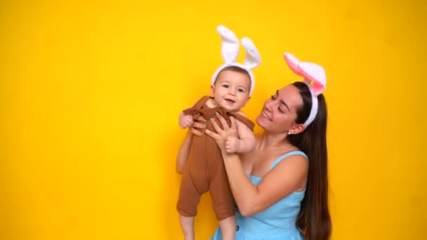 Мама і дитина з вухами кролика. Батько і дитина грають на жовтому тлі. Сім'я святкує Великдень. Симпатичний маленький хлопчик носить вуха кролика . — стокове відео