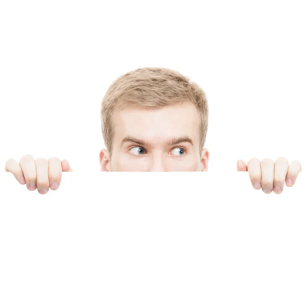Surprised young man looking from behind a board isolated on white background — Stock Photo, Image