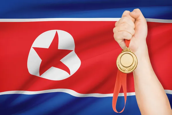 Medalj i hand med flaggan i bakgrunden - Nordkorea — Stockfoto