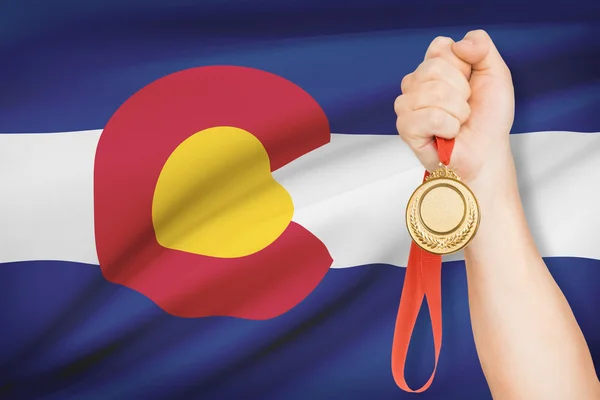 Medalj i hand med flaggan i bakgrunden - delstaten colorado. del av en serie. — Stockfoto