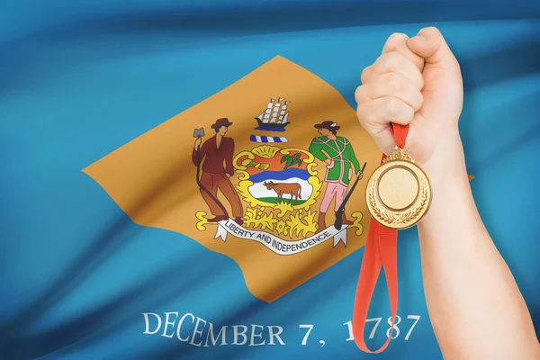Medalj i hand med flaggan i bakgrunden - delstaten delaware. del av en serie. — Stockfoto