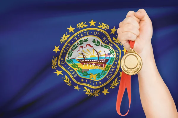 Medal in hand with flag on background - State of New Hampshire. Part of a series. — Stock Photo, Image