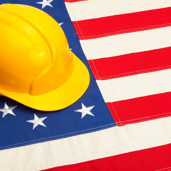 Yellow color construction helmet laying over USA flag - studio shoot - 1 to 1 ratio — Stock Photo, Image