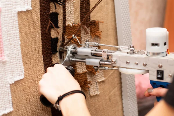 The process of making a tufting rug. Tufting a pistol in female hands against the background of a handmade brown tank rug on sacking.