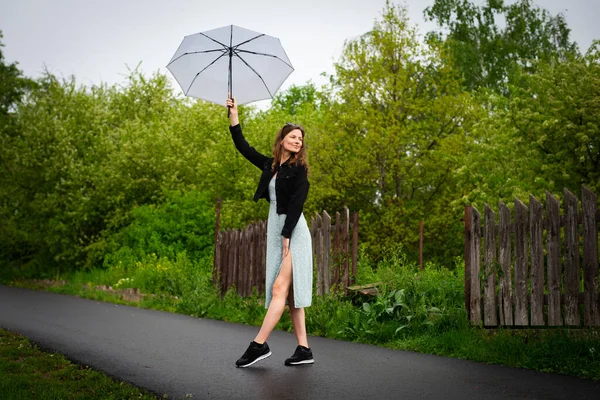 Hafif narin elbiseli güzel bir kadın yağmurlu havada hafif bir şemsiyeyle yürür..