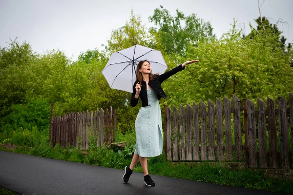Hafif narin elbiseli güzel bir kadın yağmurlu havada hafif bir şemsiyeyle yürür..