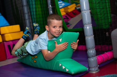 Neşeli bir çocuk, çocuk oyun merkezinde yumuşak yeşil bir timsahın üzerinde yatıyor.