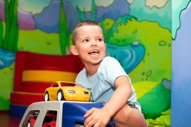 Sevimli çocuk araba taşıyıcısı ve renkli duvarlı çocuk oyun odasında arabalarla oynuyor.