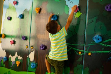 A little boy climbs up on a simulated rock in a play center