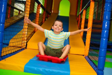 Cute child boy near a roller coaster with a plastic red sledge on the playground in the children's play center