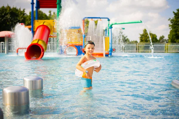 Happy laughing child in the pool at the water park. Cute boy in bright swimming trunks with an inflatable ring in the pool in the water park