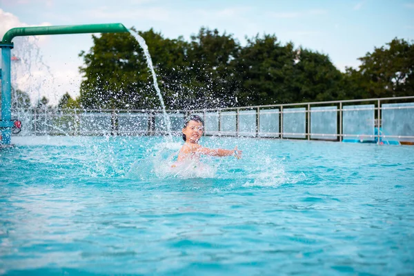 A little boy plays in the water of the water park and splashes with water. Cute boy in bright swimming trunks with an inflatable ring in the pool in the water park