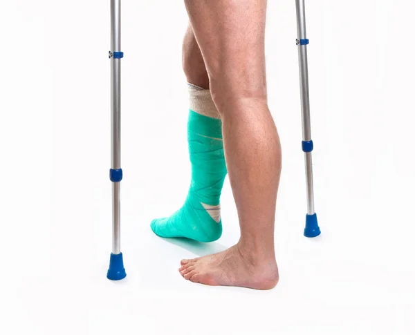 Человек со сломанной ногой с костылями на белом фоне — стоковое фото