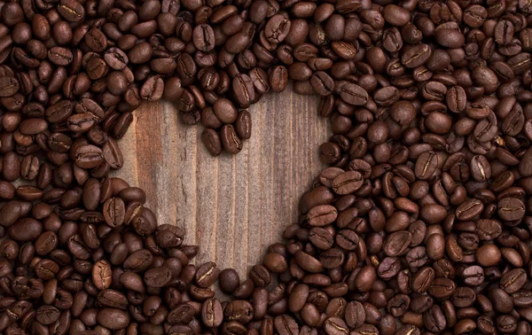 Forma de coração feito de grãos de café na mesa de madeira — Fotografia de Stock