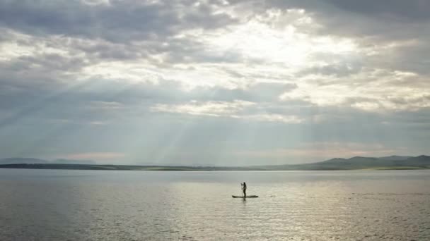Vista aérea de una mujer en un paddleboard en el mar en las montañas al atardecer — Vídeo de stock