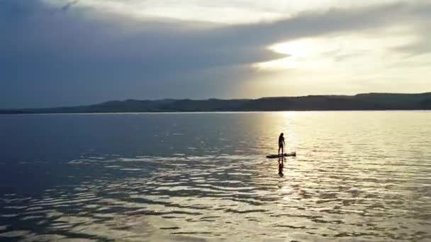Drone tiro de uma mulher com cabelo comprido surfar em um lago de montanha ao pôr do sol — Vídeo de Stock