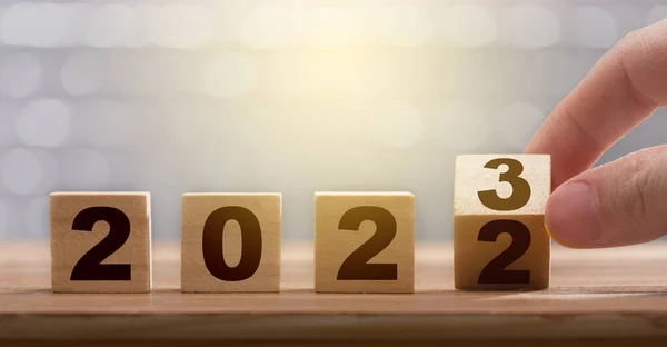 指は2022年から2023年までブロックを回します 新年のコンセプト 木製のブロックに2023年の数字 年末と開始のためのグラフィックベンダーの仕事 ロイヤリティフリーのストック画像