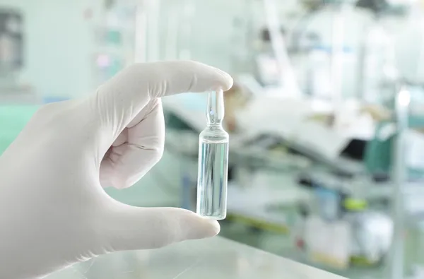 Ampolla en la mano de los trabajadores médicos contra la sala hospitalaria —  Fotos de Stock