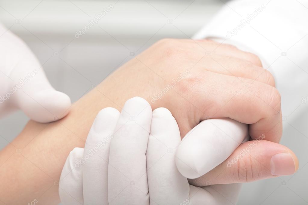 Doctor in white gloves gently holds the patient's arm