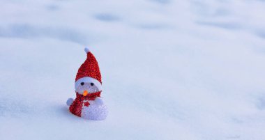 Karlı Noel bayrağı ve kırmızı atkı ve şapkalı bir kardan adam, kışın kar yığınında bir oyuncak kardan adam.