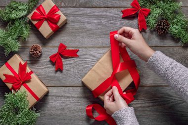 Yılbaşı hediyeleri, arka plan, el çantası, hediyeye fiyonk bağlama, ağaç bir masanın üzerinde köknar dalları, koniler ve kurdeleler.