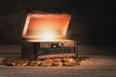 Masanın üzerinde bozuk paralar olan eski tahta sandık, sandık açık, içeriden parlak bir ışık, peri masalı, gizem, korsan hazinesi, zenginlik, pandora 'nın kutusu konsepti