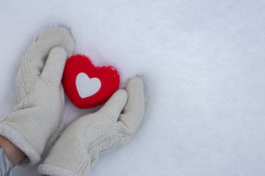 Kış günü, kar üzerinde kırmızı bir kalple örülmüş eldiven giymiş kadınların elleri. Aşk konsepti. Sevgililer Günü geçmişi